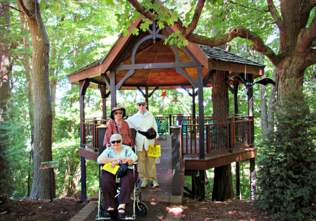 Senior adults posing for photo outside treehouse, Bookworm Gardens