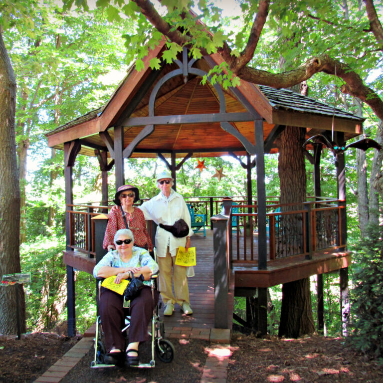 Senior adults posing for photo outside treehouse, Bookworm Gardens